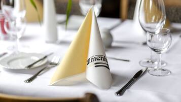Una mesa con mantel blanco, servilleta dorada, tenedor de plata, cuchillo de plata y copa de cristal.