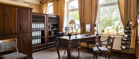 Une pièce avec un bureau en bois, des chaises, une bibliothèque et une grande fenêtre avec des rideaux.