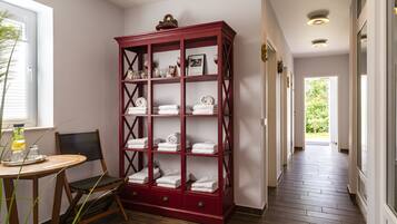 A hallway with a red wooden cabinet filled with towels, a wooden chair, and a small table with a drink.
