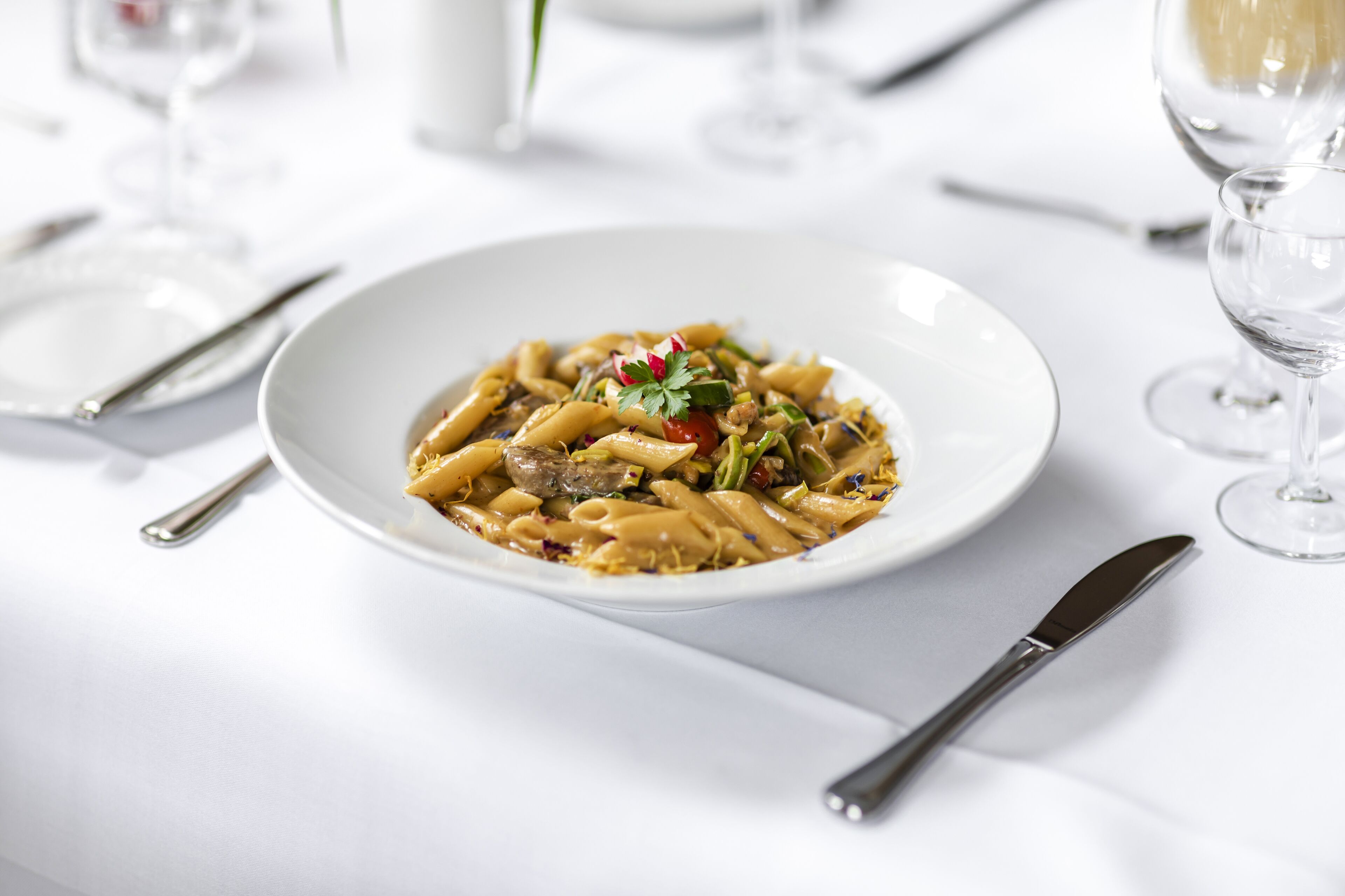 A white plate of pasta with a garnish on a white table.