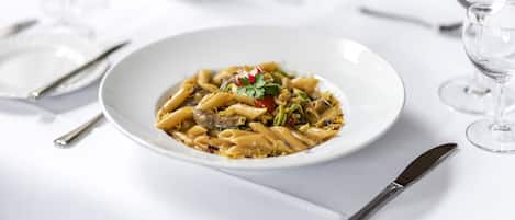 A white plate of pasta with a garnish on a white table.