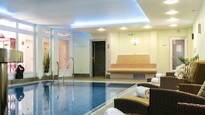 A hotel lobby with a swimming pool, wicker furniture, and a reception area. - Villa Ulmenhof (Bredstedt)