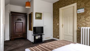 A hotel room with a bed, a TV on a stand, a wardrobe, and a door with a radiator.