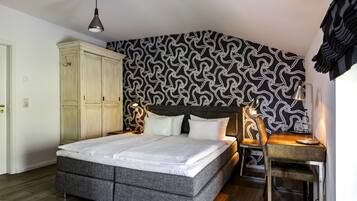 A bedroom with a bed, a desk, and a chair. There is a wardrobe and a patterned wall.