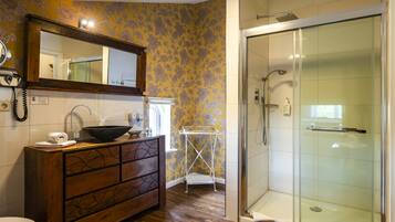 A bathroom with a wooden vanity, a mirror, a sink, a shower, and a tiled floor.