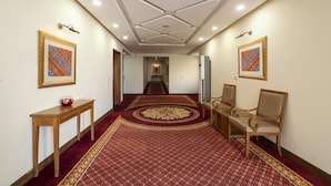 A hallway with patterned carpet, wooden furniture, and framed artwork on the walls. - Hotel One Sukkur (Sukkur)