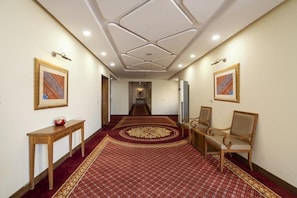 A hallway with patterned carpet, wooden furniture, and framed artwork on the walls. - Hotel One Sukkur (Sukkur)
