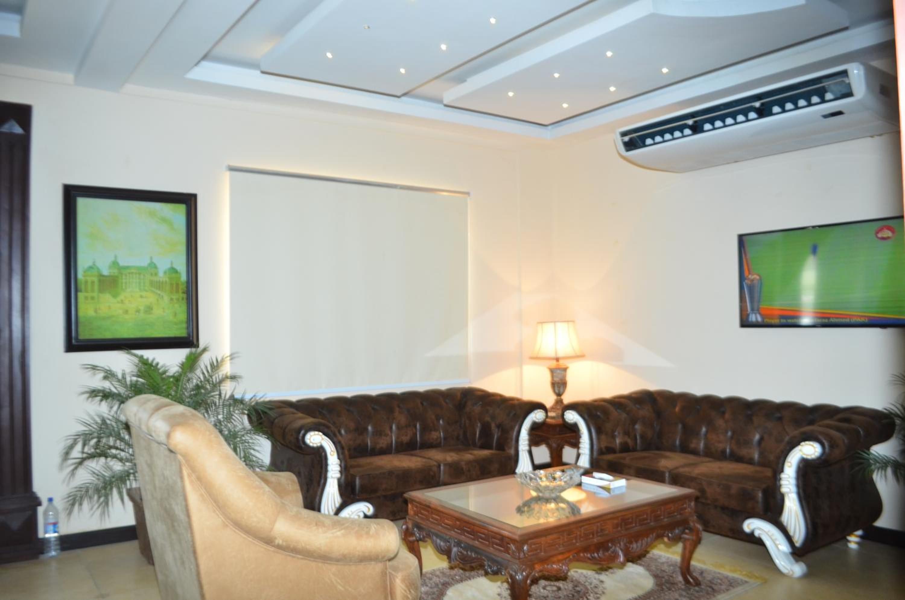 Uma sala de estar com sofá de couro marrom, poltrona bege, mesa de centro de vidro, luminária e quadro na parede.