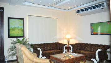 Uma sala de estar com sofá de couro marrom, poltrona bege, mesa de centro de vidro, luminária e quadro na parede.
