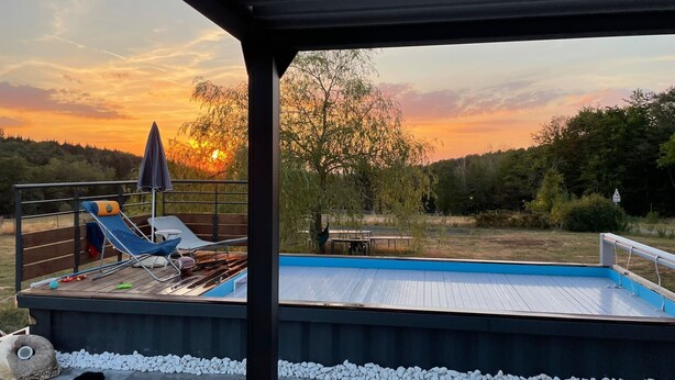 A swimming pool with a wooden deck, lounge chairs, and a table. - Cosy villa in wooded surroundings Heated swimming pool available from May to September (Angomont)