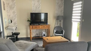 A modern living room with a grey sofa, a wooden coffee table, a TV on a stand, and a lamp. - Cosy villa in wooded surroundings Heated swimming pool available from May to September (Angomont)