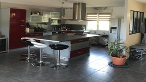 A modern kitchen with a central island, bar stools, stainless steel appliances, and a potted plant. - Cosy villa in wooded surroundings Heated swimming pool available from May to September (Angomont)