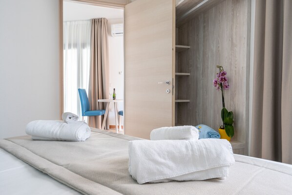 Una habitación de hotel con una cama, una silla, una mesita, una planta en maceta y un armario.