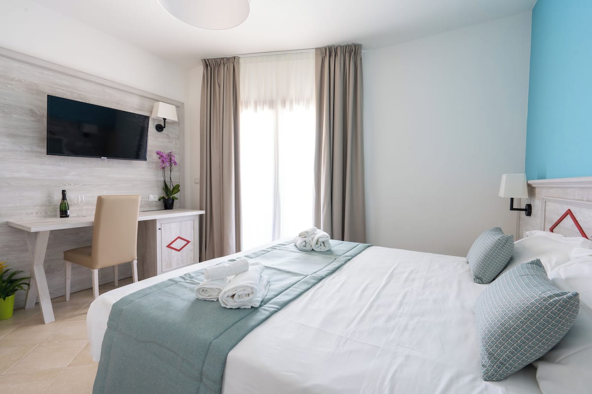 A hotel room with a bed, a desk, a chair, a TV, and a window with curtains.