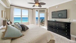 Ein Schlafzimmer mit Bett, Kommode, Deckenventilator, Fernseher und Meerblick.