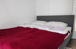 Comfortable bed with a cozy red blanket and patterned pillows, situated against a neutral background.
