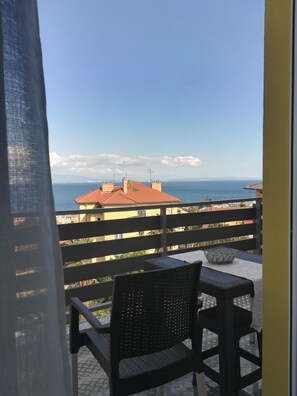 Un balcón con vista al mar, una silla y una mesa.