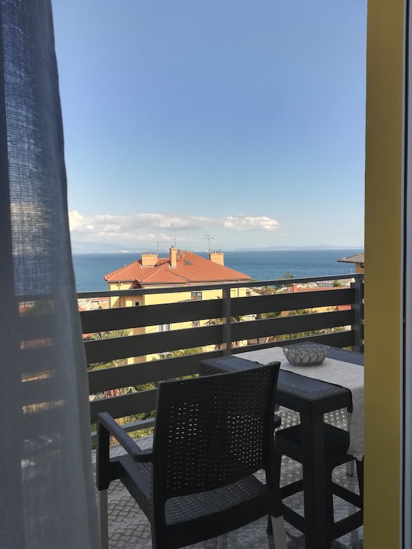 Enjoy the ocean view from this balcony with a wicker chair and metal railing.