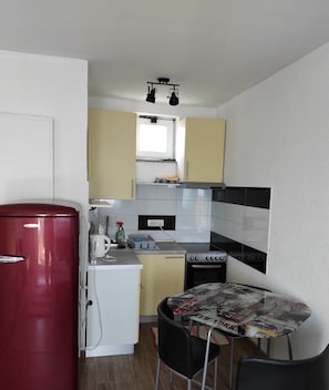 Compact kitchen with modern design, featuring a refrigerator, stove, sink, and dining area with table and chairs.