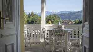 An open balcony with a view of mountains, a table with chairs, and a decorative fence. - Apartment Blue (Pörtschach)
