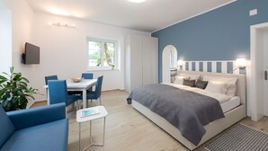 A modern bedroom with a large bed, a dining area with chairs, a small table, and a TV mounted on the wall. - Apartment Blue (Pörtschach)