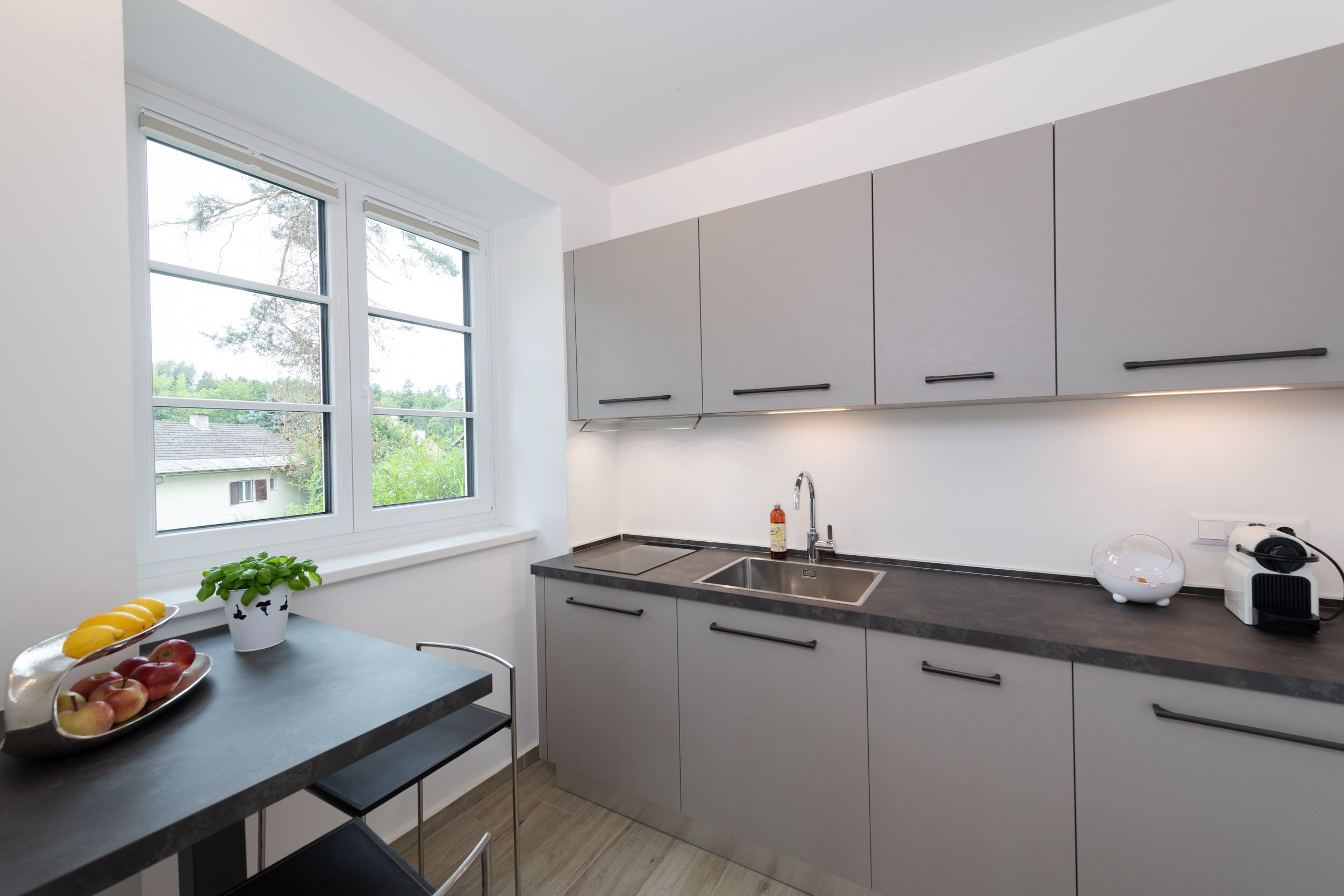 Cocina moderna con armarios grises, encimera negra, un lavabo y una ventana con vistas al exterior.