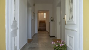 A hallway with a staircase leading to an upper floor, white doors, and a potted plant with pink flowers. - Apartment Blue (Pörtschach)