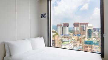 A hotel room with a large window offering a city view.