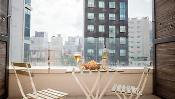 A balcony with a table set for two, featuring a glass of beer, a bottle, and a basket of snacks.