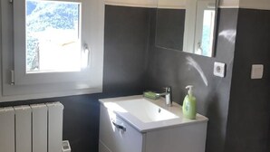 Ein modernes Badezimmer mit einem weißen Waschtisch, einem großen, beleuchteten Spiegel, einem Fenster und einer Heizung.