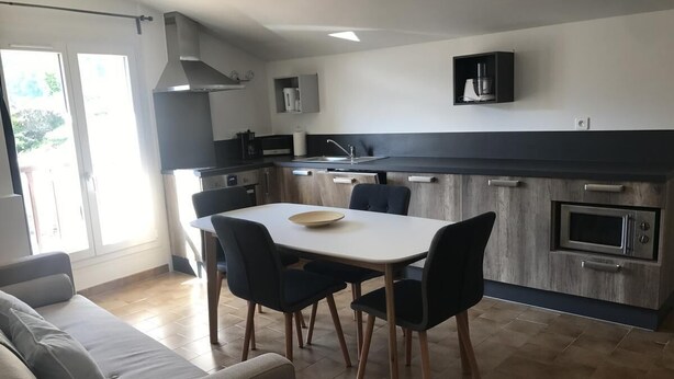 Eine moderne Küche mit Essbereich, ausgestattet mit einem großen Tisch, Stühlen, einem eingebauten Backofen und einer Kaffeemaschine.