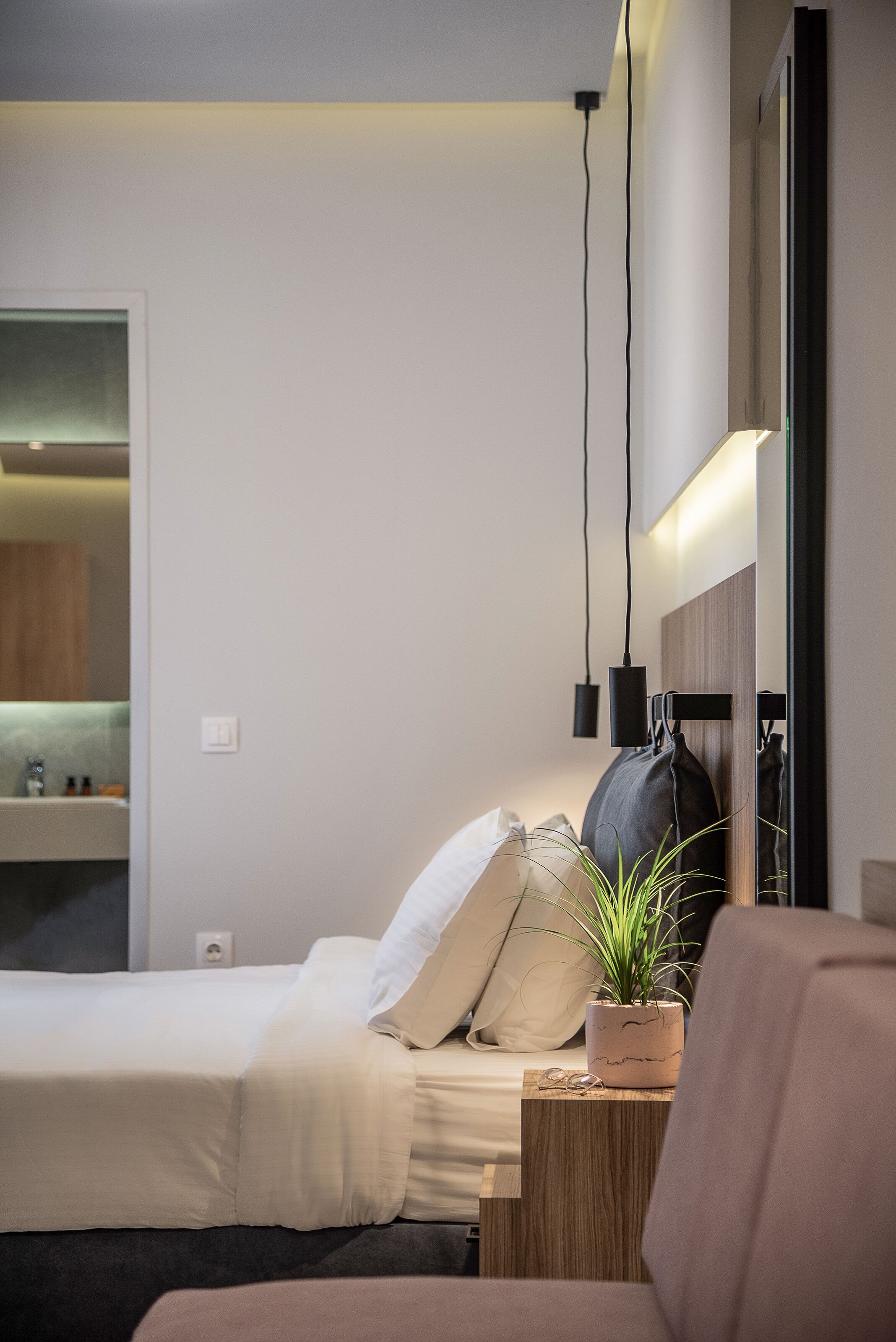 A modern hotel room with a bed, bedside table, potted plant, and a mirror.