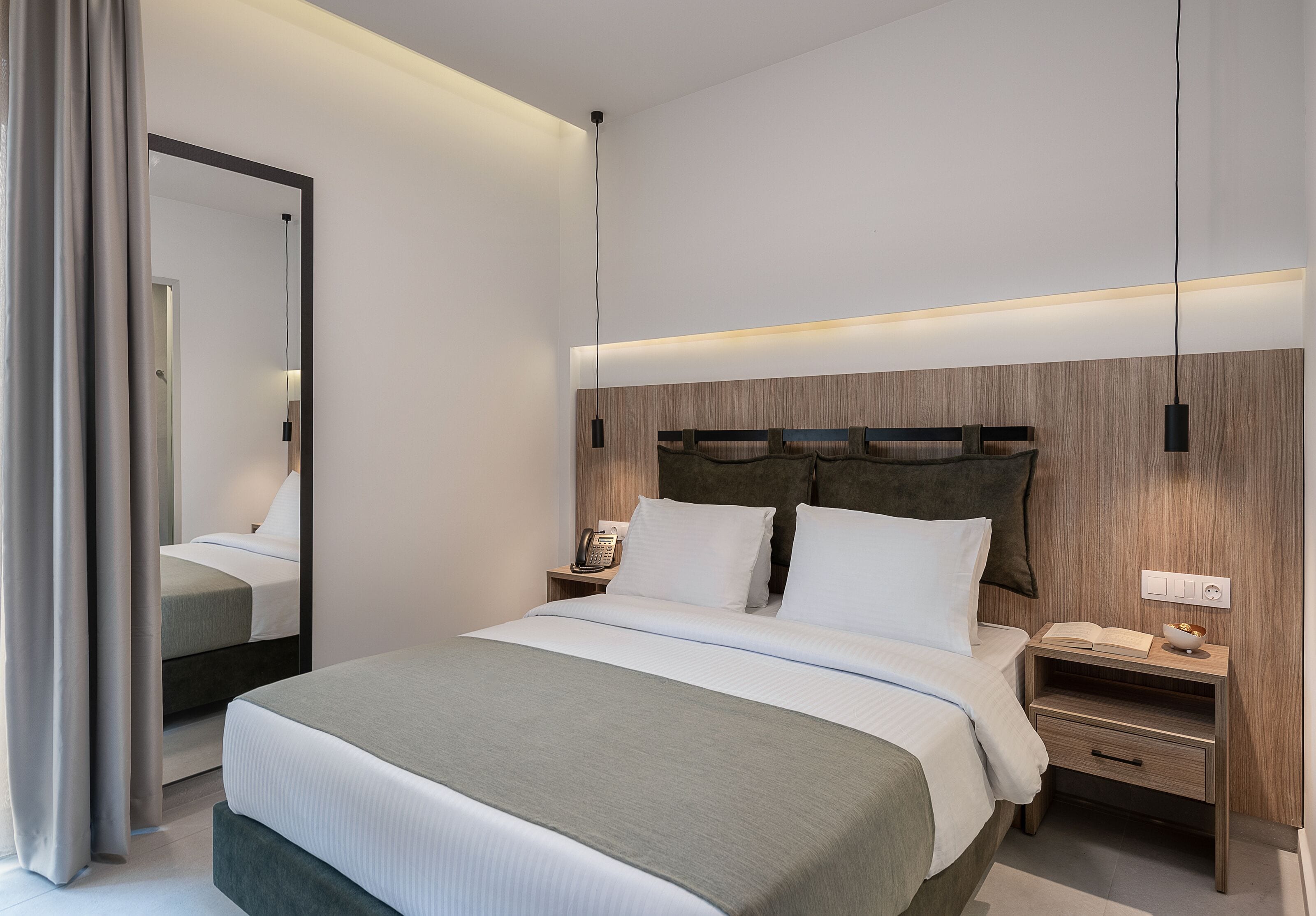 A modern hotel room with a large bed, bedside tables, a mirror, and a wooden headboard.