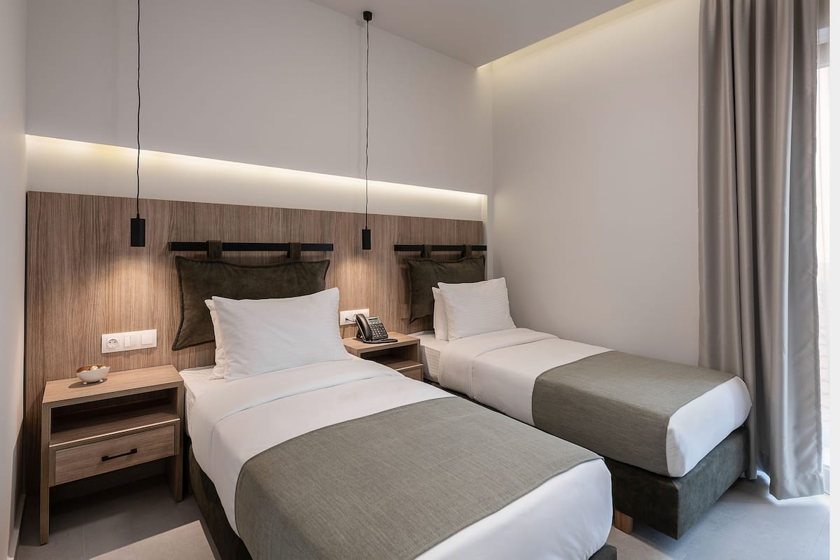 Ein modernes Hotelzimmer mit zwei Einzelbetten, einem Holzkopfteil, Nachttischen mit Lampen und einem Telefon.