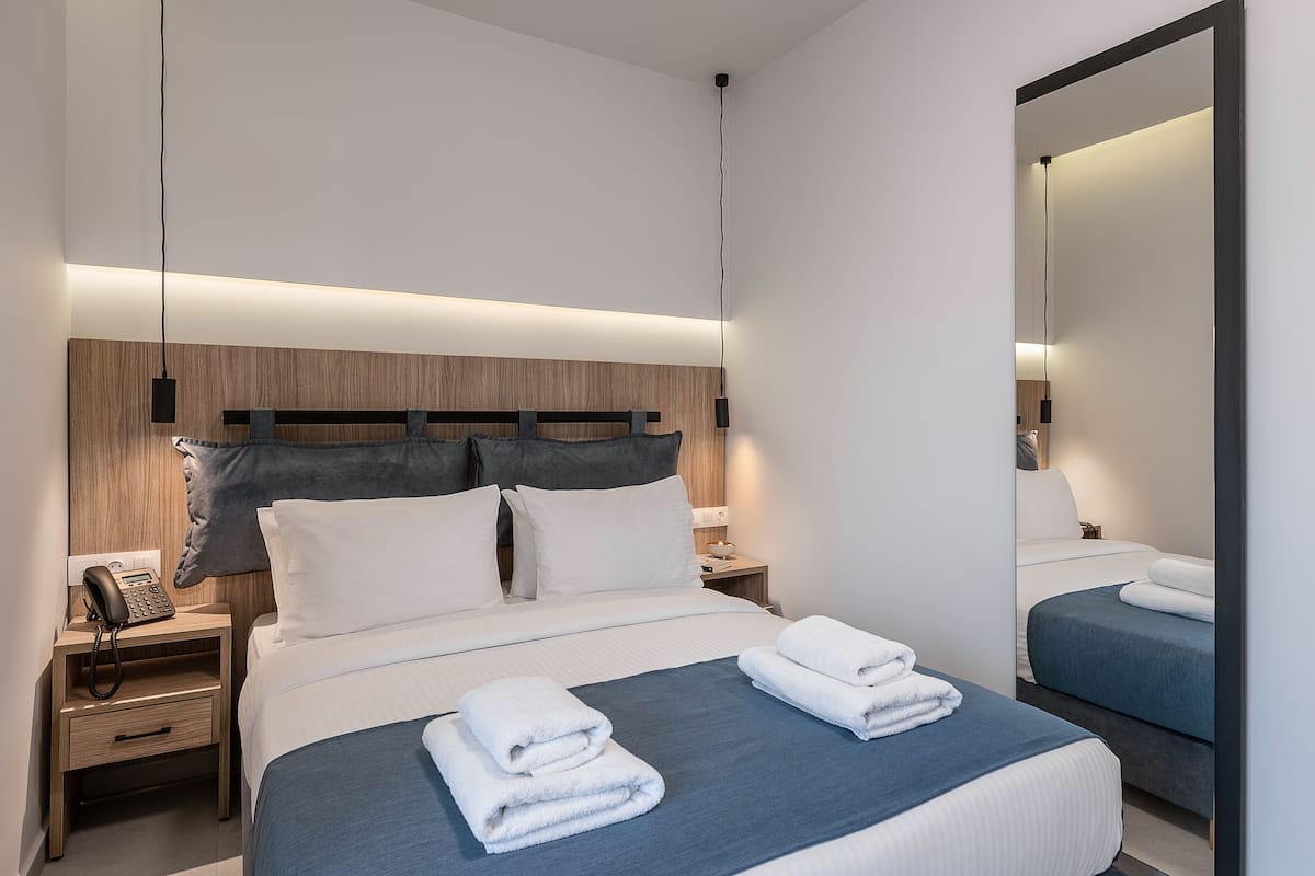 Ein modernes Hotelzimmer mit einem ordentlich bezogenen Bett, einem Nachttisch mit Telefon und einem großen Spiegel.