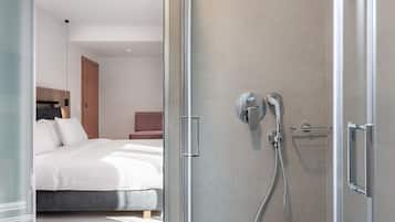 A modern hotel room with a glass shower enclosure, a bed with white linens, and a bedside table with a lamp.