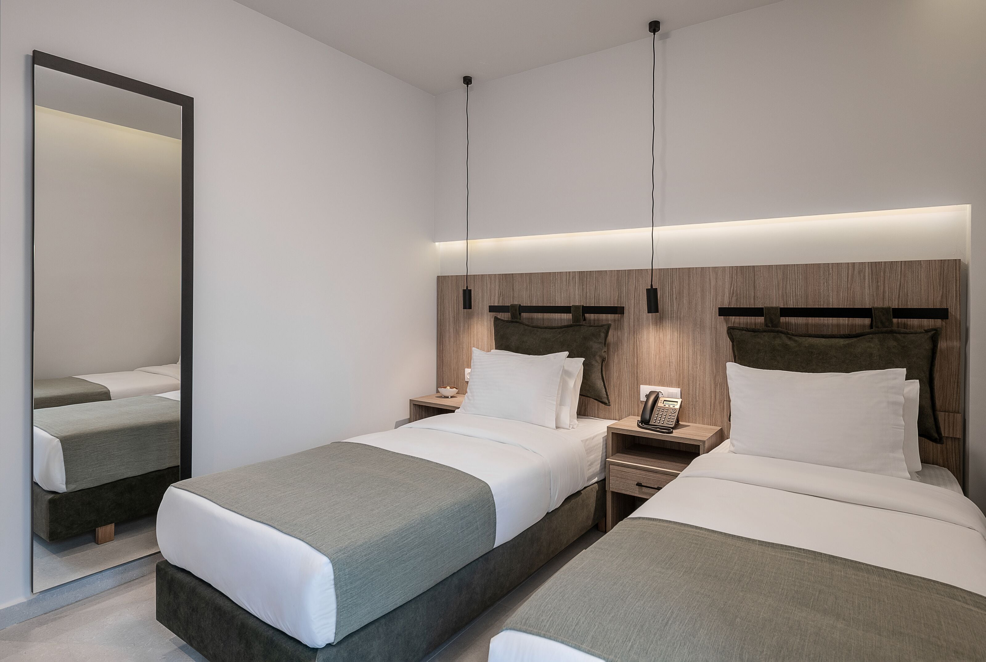 Ein modernes Hotelzimmer mit zwei Betten, einem großen Spiegel, Nachttischen und einem Holzkopfteil.