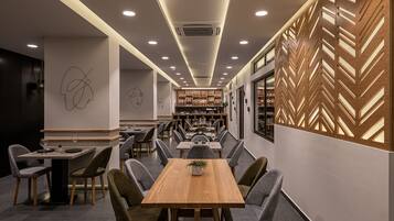 A modern restaurant with a long dining table, multiple chairs, and a bar area in the background.