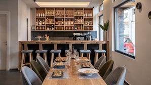Een restaurant met een lange houten tafel gedekt voor een maaltijd, omringd door stoelen, en een barzone met flessen en glazen op de planken.