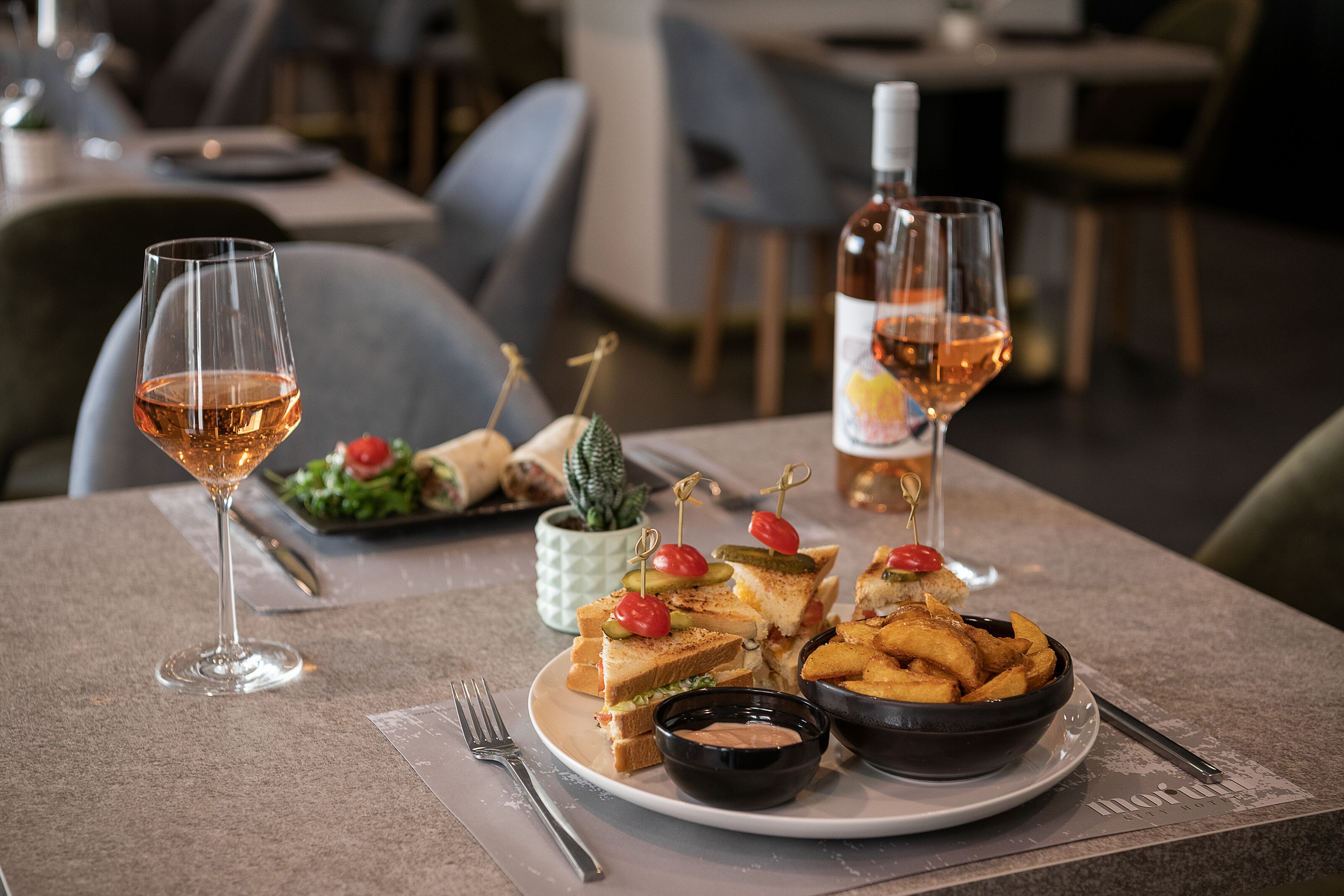 Une table à manger avec une assiette de sandwichs, un bol de frites et deux verres de vin.