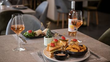 Une table à manger avec une assiette de sandwichs, un bol de frites et deux verres de vin.