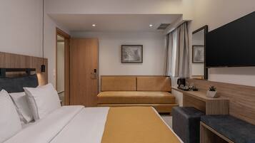 A modern hotel room with a large bed, a sofa, a desk, and a flat-screen TV.