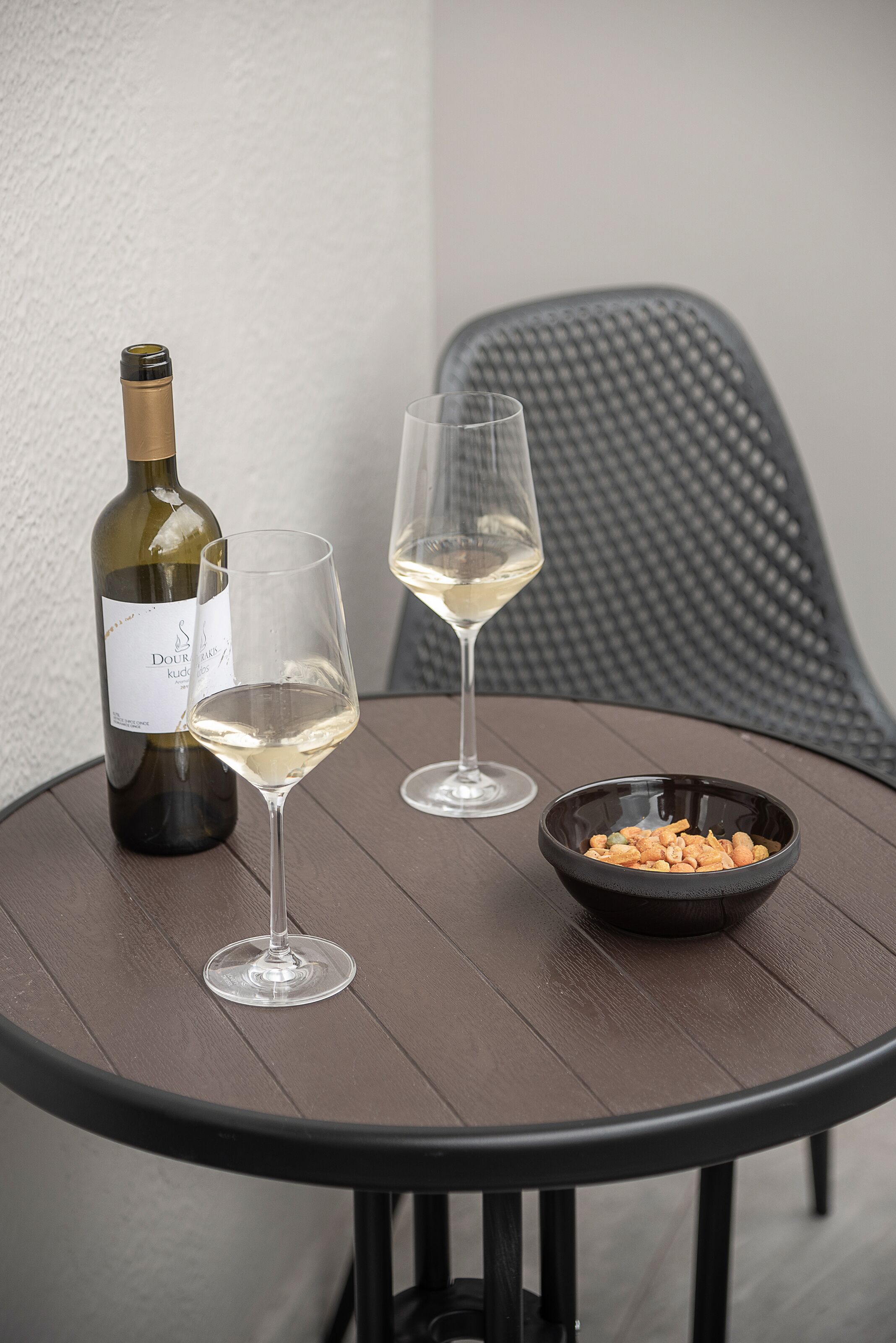 A round table with a bottle of wine, two glasses, and a bowl of snacks.