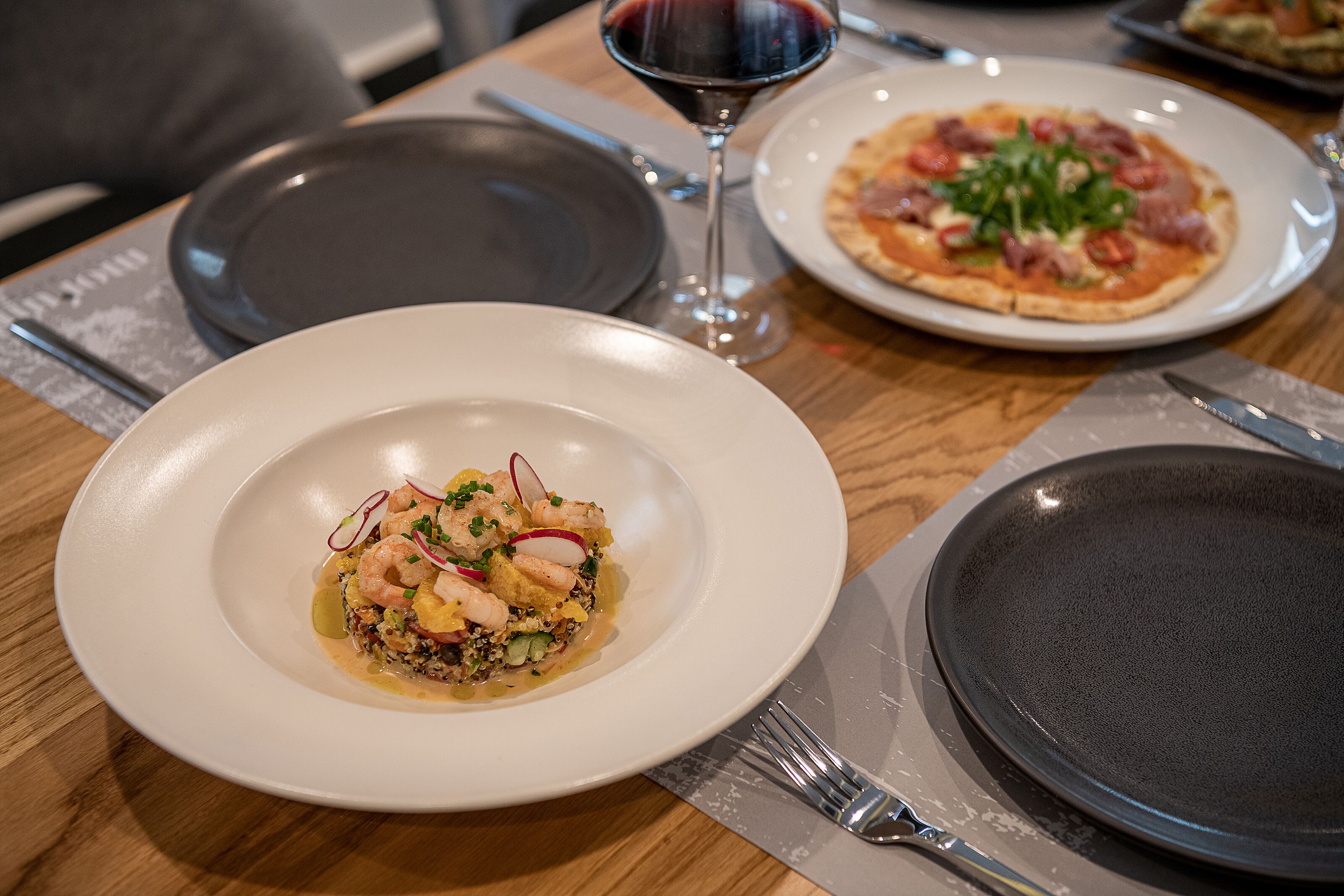 A dining table with plates of food, a wine glass, and cutlery.