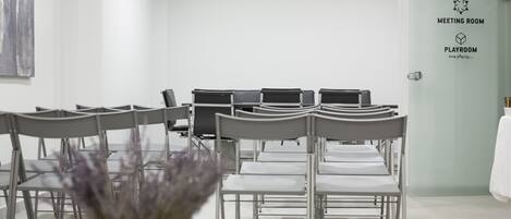 A meeting room with rows of chairs and a projector screen. There is a sign indicating a meeting room and a playroom.