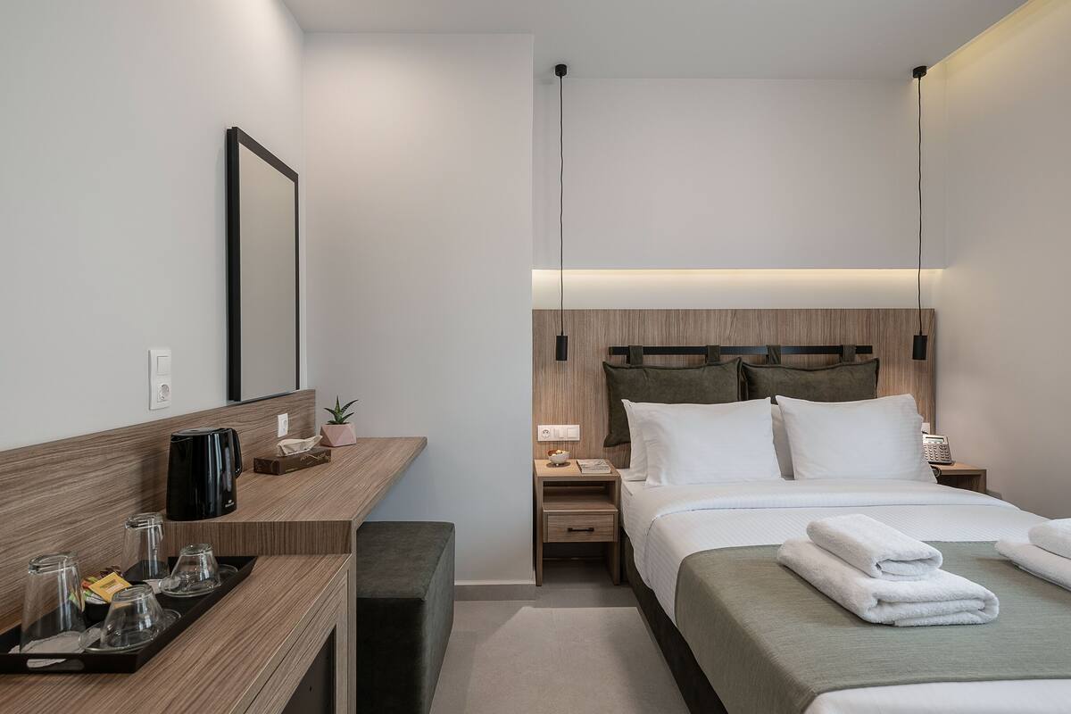 Ein modernes Hotelzimmer mit einem Holztisch, einem Bett mit weißer Bettwäsche, einem Nachttisch mit Lampe und einem großen Spiegel an der Wand.