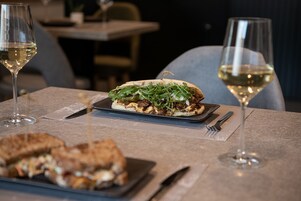 A dining table with a sandwich and two glasses of white wine.