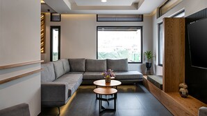 Een moderne woonkamer met een grijze hoekbank, een ronde houten salontafel en een grote flatscreen televisie.