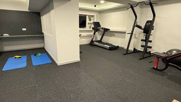 A home gym with a treadmill, weight bench, and exercise mats.