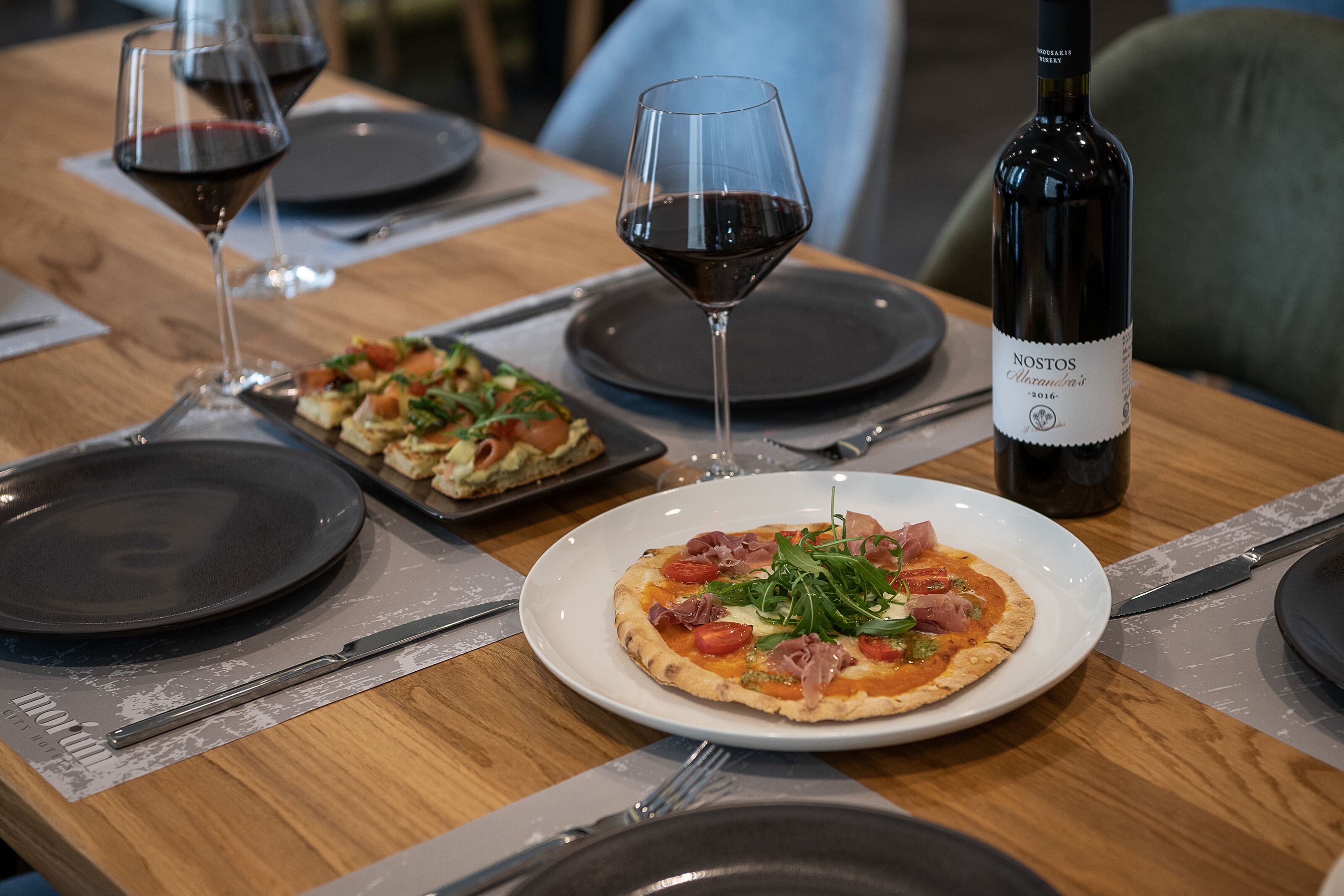 A dining table with two plates of pizza, wine glasses, and a bottle of wine.